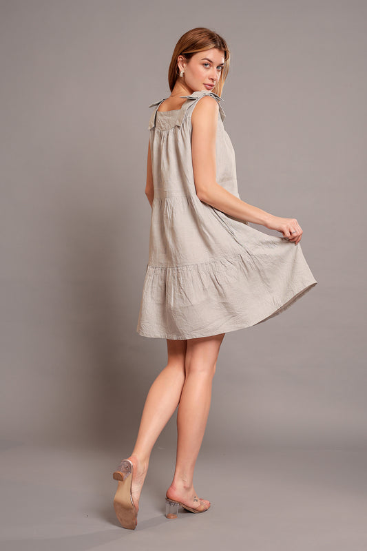 Woman wearing a light gray sleeveless linen mini dress against a plain background.