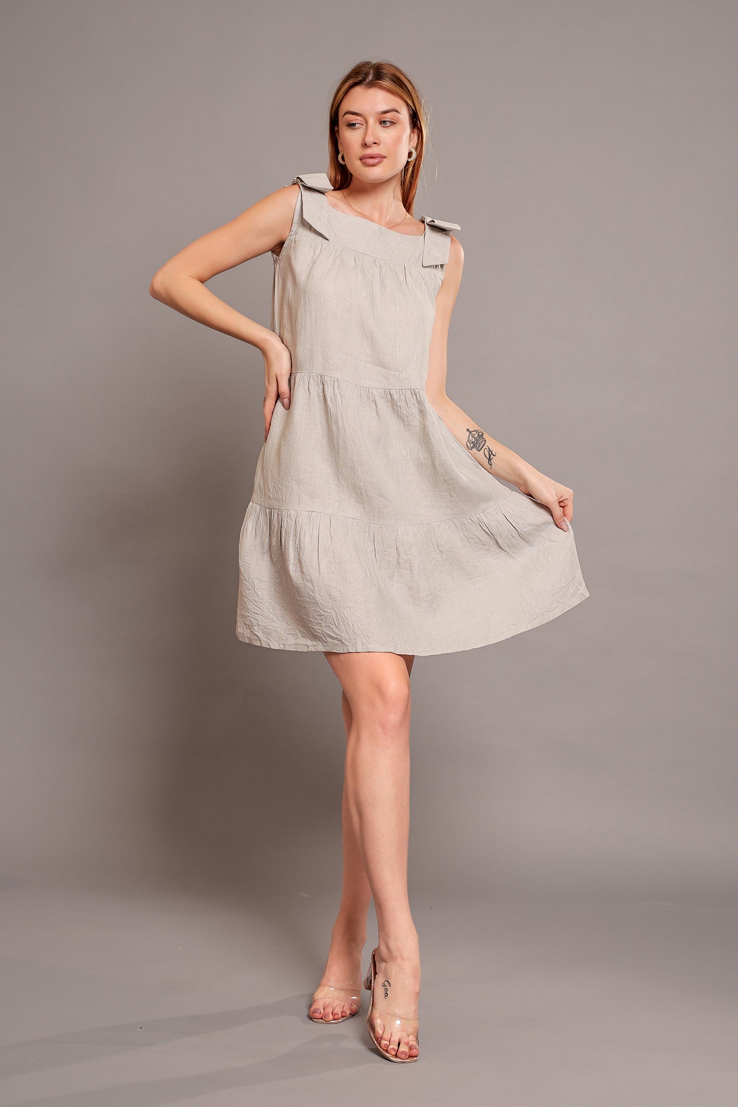 Woman wearing a beige sleeveless linen mini dress against a gray background.