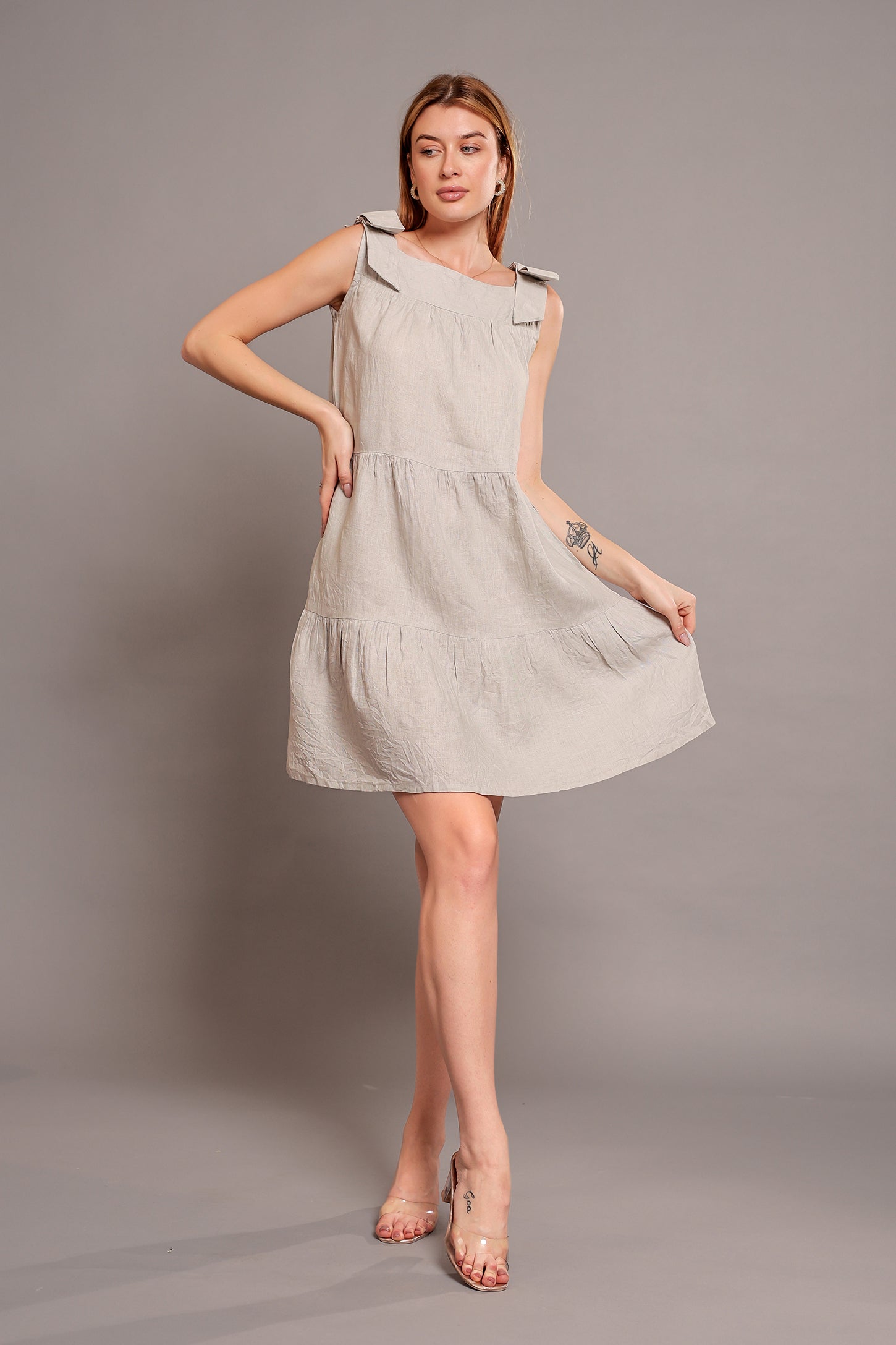 Woman wearing a beige sleeveless linen mini dress against a gray background.