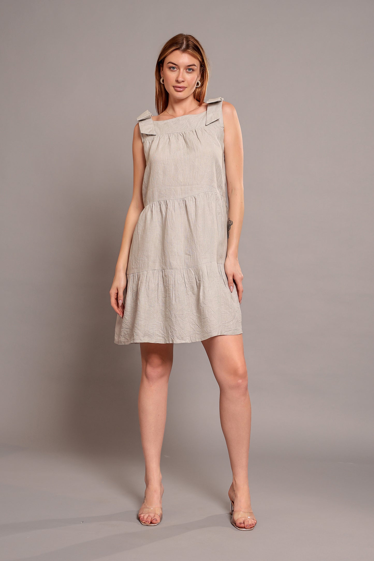 Woman wearing a beige sleeveless linen mini dress against a plain background.