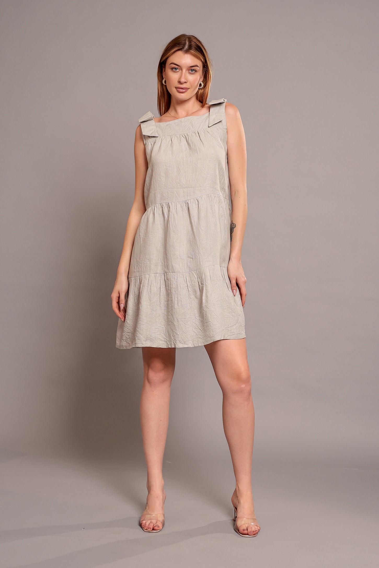 Woman wearing a beige sleeveless linen mini dress against a plain background.