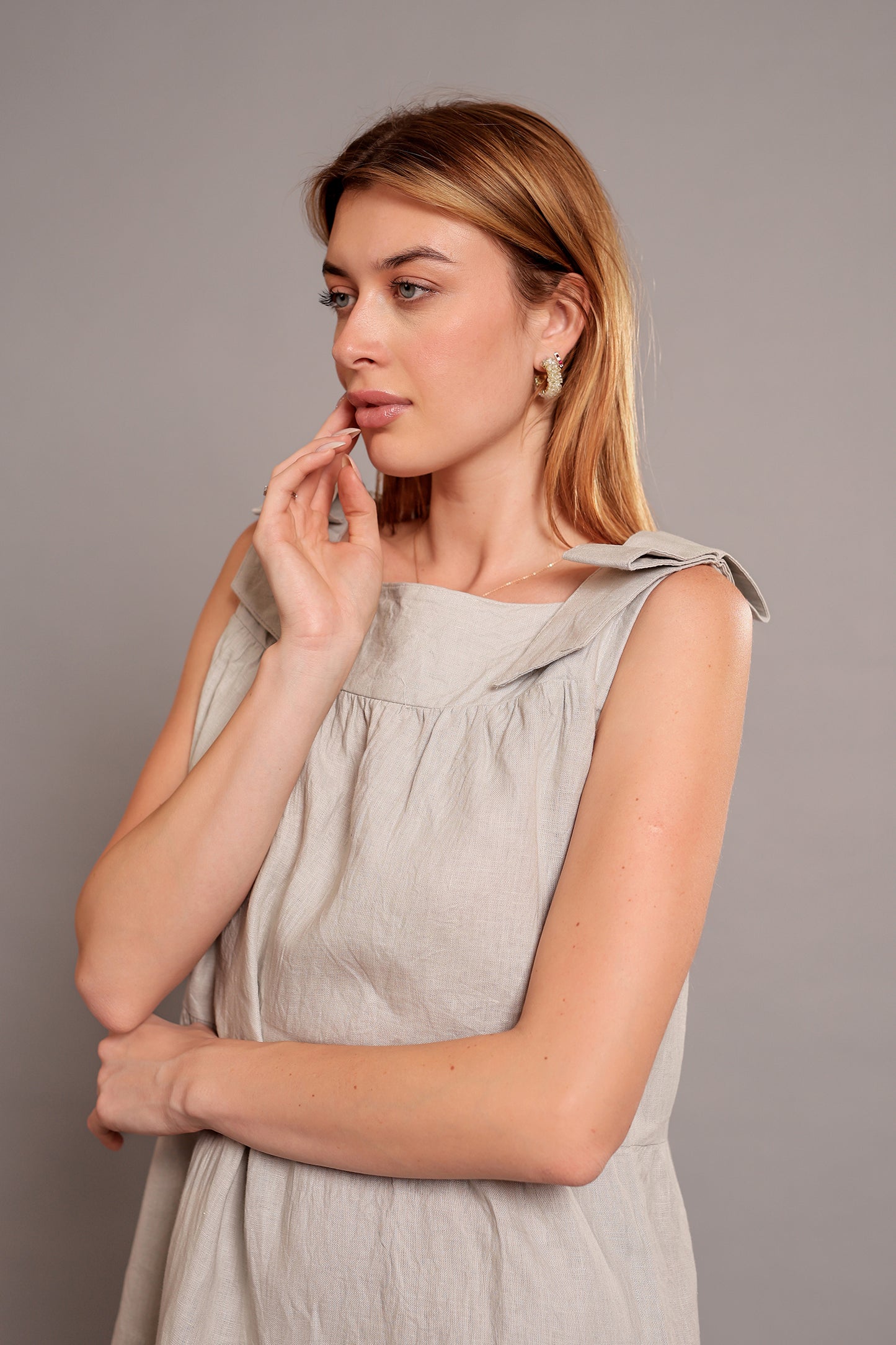 Woman wearing a light gray sleeveless linen mini dress against a plain background.