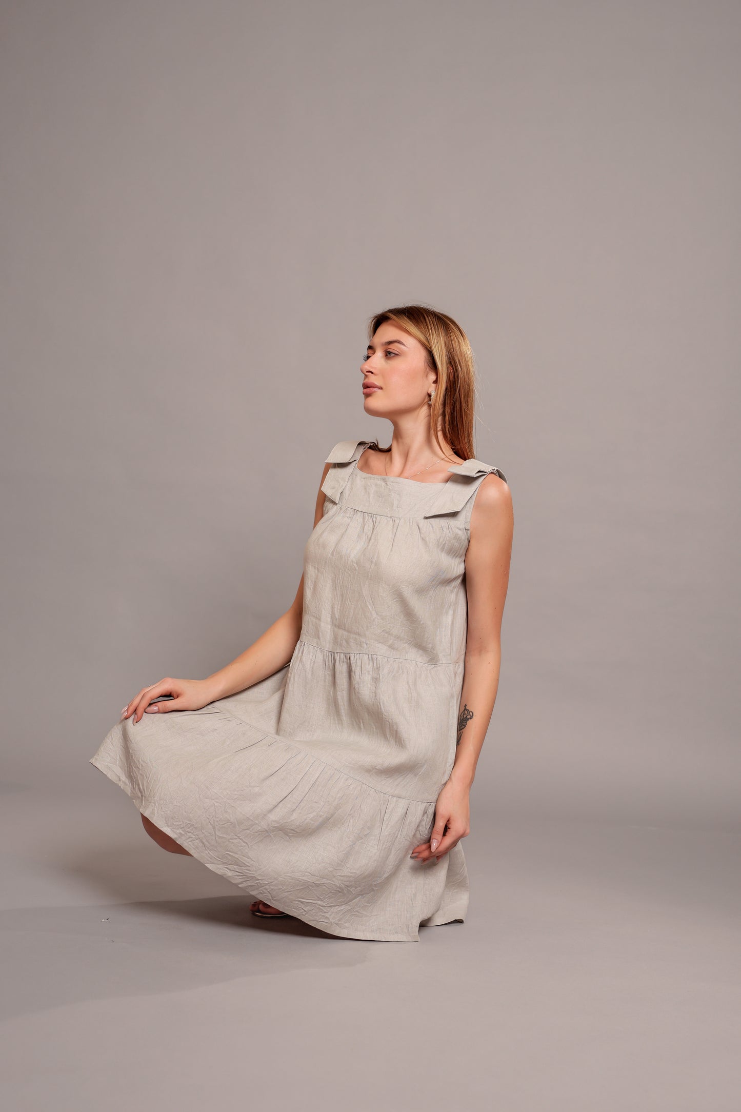 Woman wearing a beige sleeveless linen mini dress against a gray background.