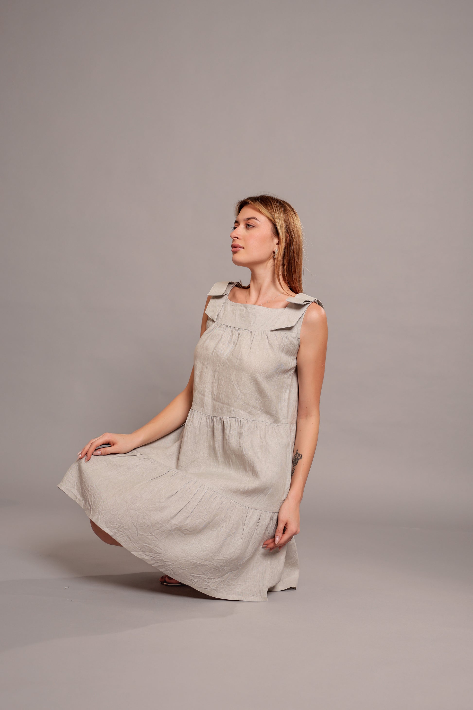Woman wearing a beige sleeveless linen mini dress against a gray background.
